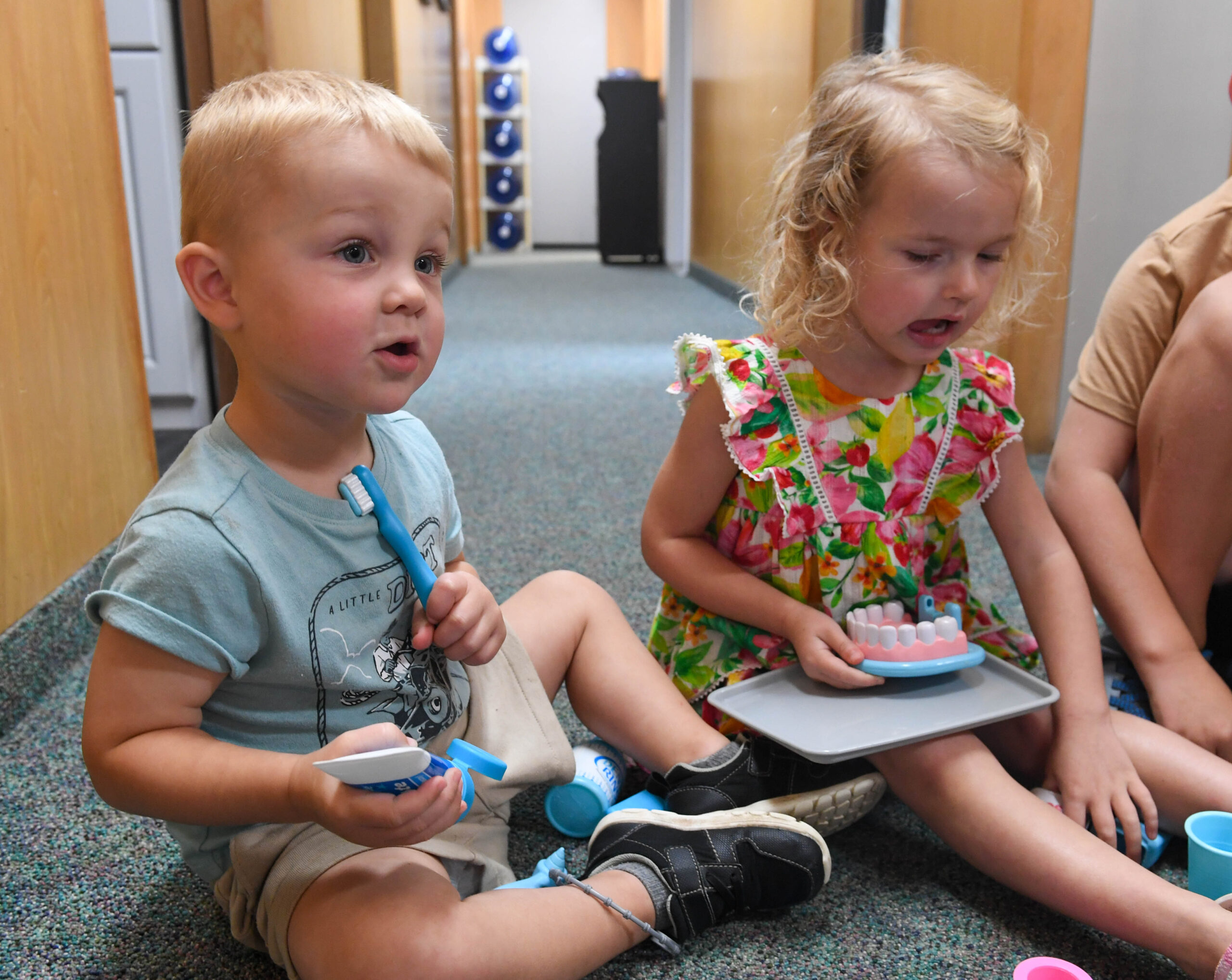 Two children playing with a playset of fake teeth in the waiting room of a dentist office